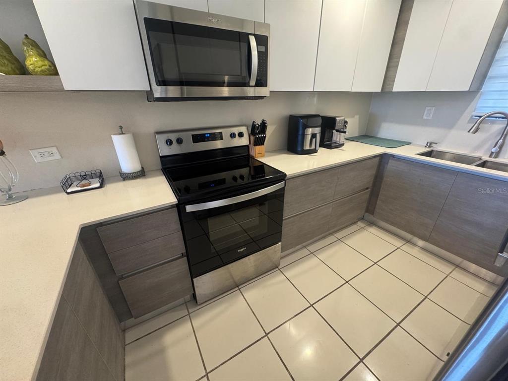 A kitchen features white upper cabinets, wood-grain lower cabinets, stainless steel appliances, and tiled flooring — 295 PALMAS INNWAY UNIT 323, HUMACAO, PR
