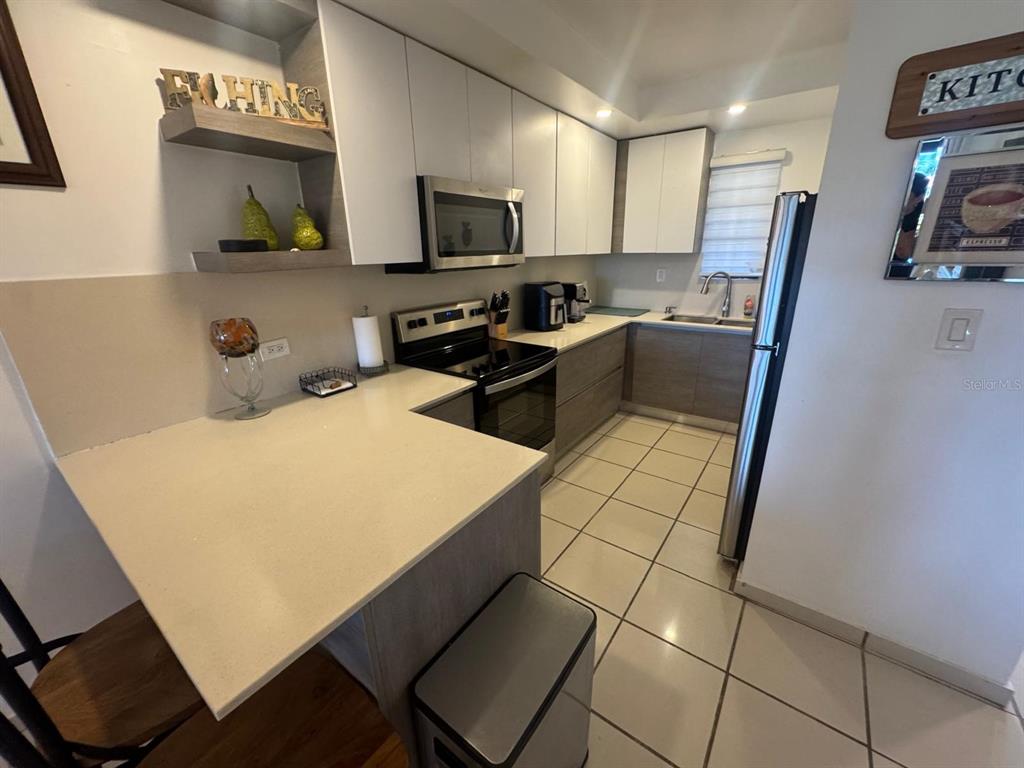 A modern kitchen features white upper cabinets, wood-tone lower cabinets, and light-colored tile flooring — 295 PALMAS INNWAY UNIT 323, HUMACAO, PR