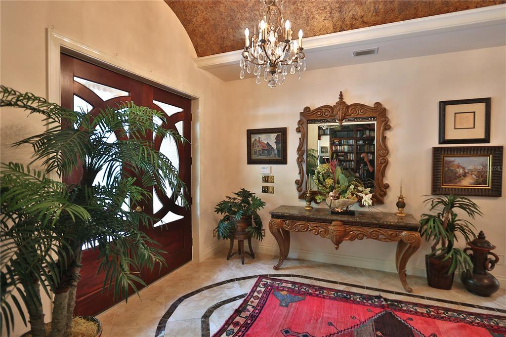 An elegant foyer features a crystal chandelier, a marble-topped console table, and a red rug — 1300 SW 43RD PLACE, OCALA, FL