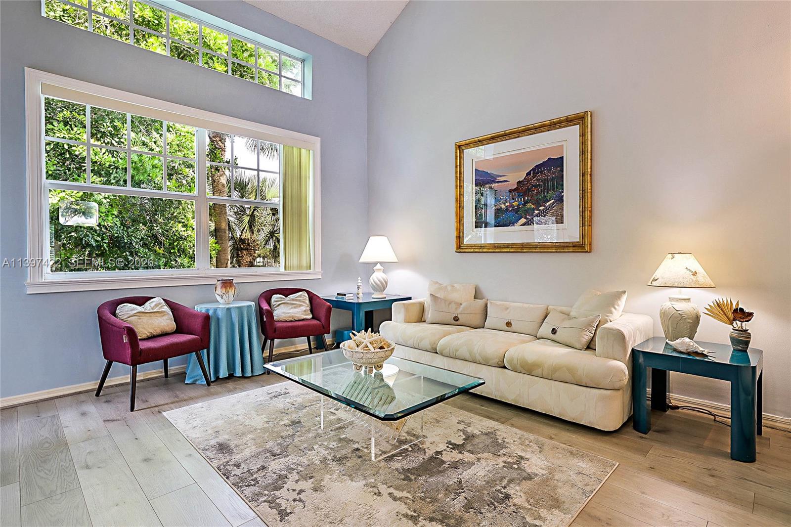 A living room features a vaulted ceiling, large windows, a beige sofa, and two burgundy chairs — 905 Mainsail Circle # 905, Jupiter FL 33477, JUPITER, FL