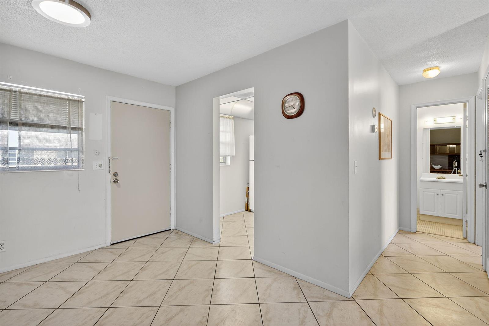 An interior view shows a tiled entryway with a front door, a clock, and a bathroom — 2152 NE 1st Way # 205, Boynton Beach FL 33435, BOYNTON BEACH, FL