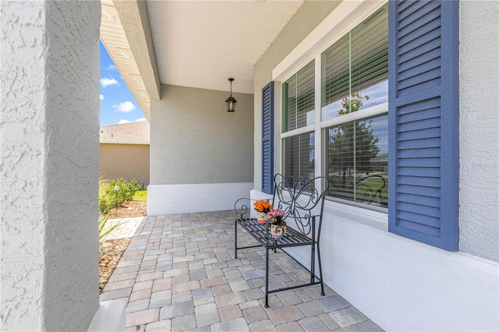 A covered front porch features a paved floor, a metal butterfly bench, and blue shutters — 10458 SW 98TH PLACE ROAD, OCALA, FL
