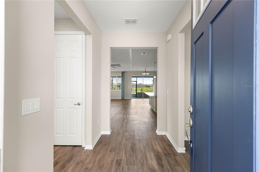 A view from an open blue front door into a hallway with wood-look flooring — 10458 SW 98TH PLACE ROAD, OCALA, FL