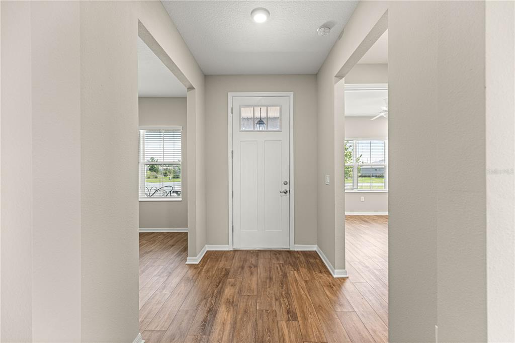An entryway with light-colored walls, wood-look flooring, and a white front door with glass panels — 10458 SW 98TH PLACE ROAD, OCALA, FL