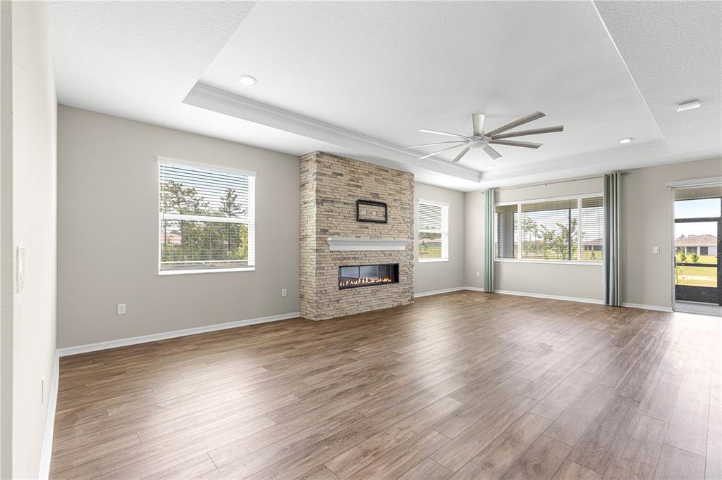 A living room features light wood-look flooring, a stone fireplace, and a tray ceiling — 10458 SW 98TH PLACE ROAD, OCALA, FL
