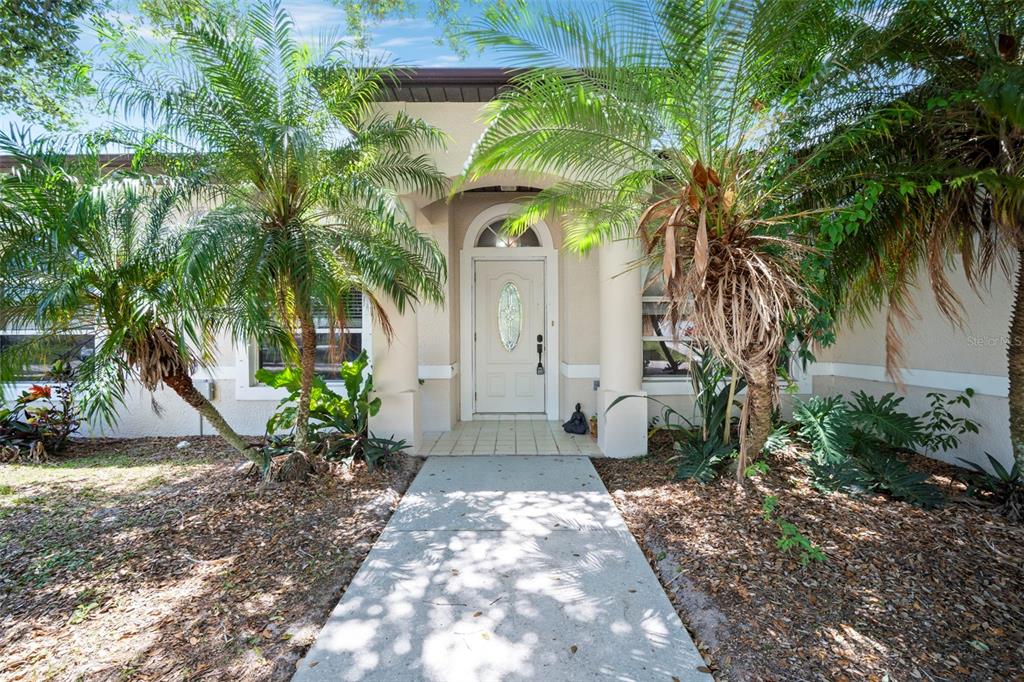 A concrete walkway leads to the front entrance of a house framed by palm trees — 1724 BARKER STREET NE, PALM BAY, FL