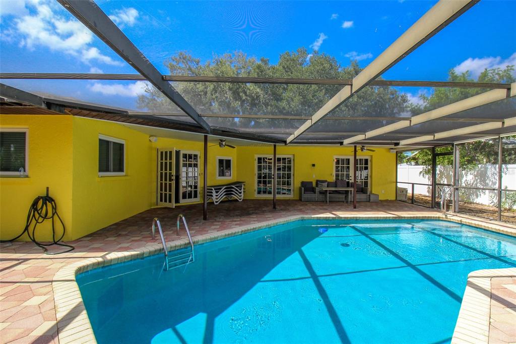 A bright yellow house exterior features a screened-in pool and a paved patio area — 2807 67TH STREET W, BRADENTON, FL