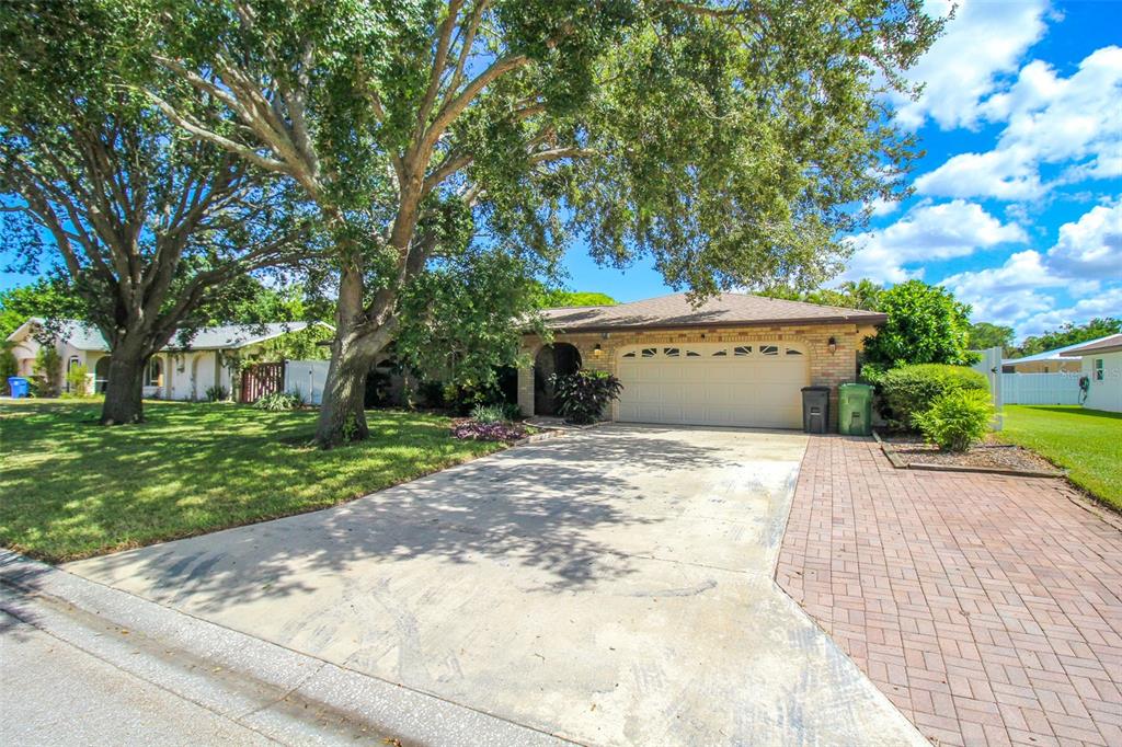 A single-story brick house with a two-car garage, concrete driveway, and large shade trees — 2807 67TH STREET W, BRADENTON, FL