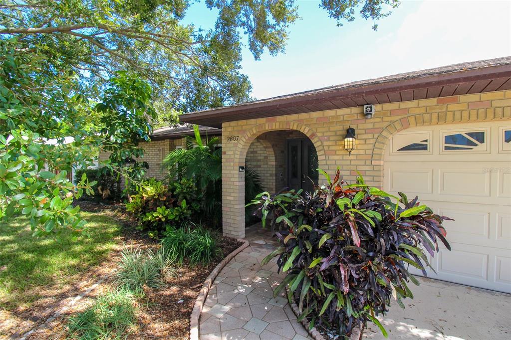 A brick house exterior features an arched entryway, a paved walkway, and a white garage door — 2807 67TH STREET W, BRADENTON, FL