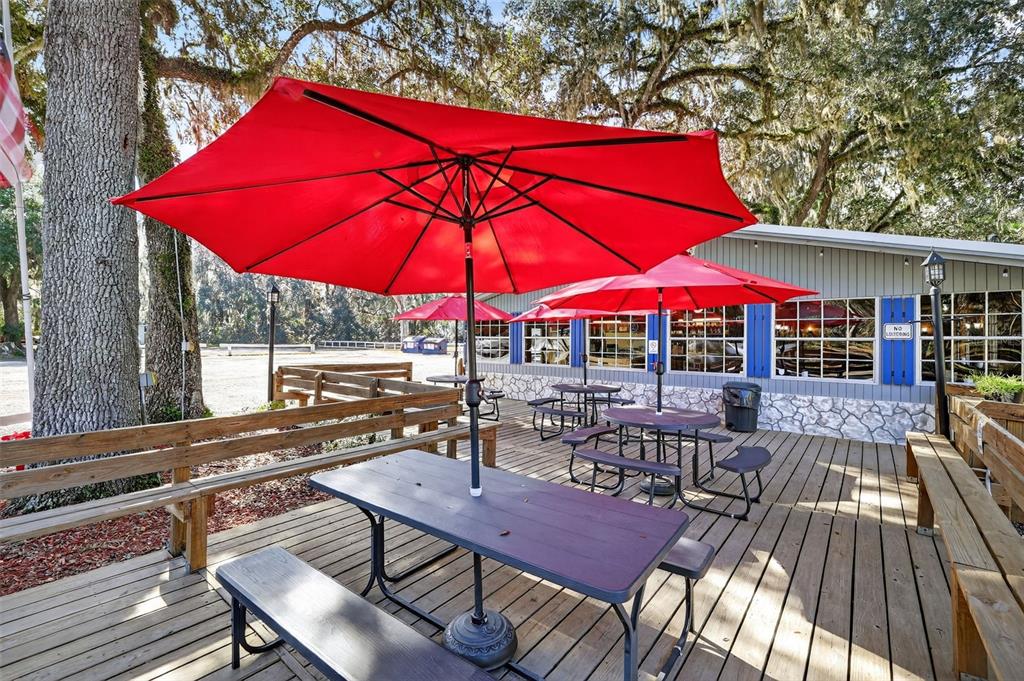 An outdoor wooden deck features several picnic tables with red umbrellas under large oak trees — 2396 N C 470, LAKE PANASOFFKEE, FL