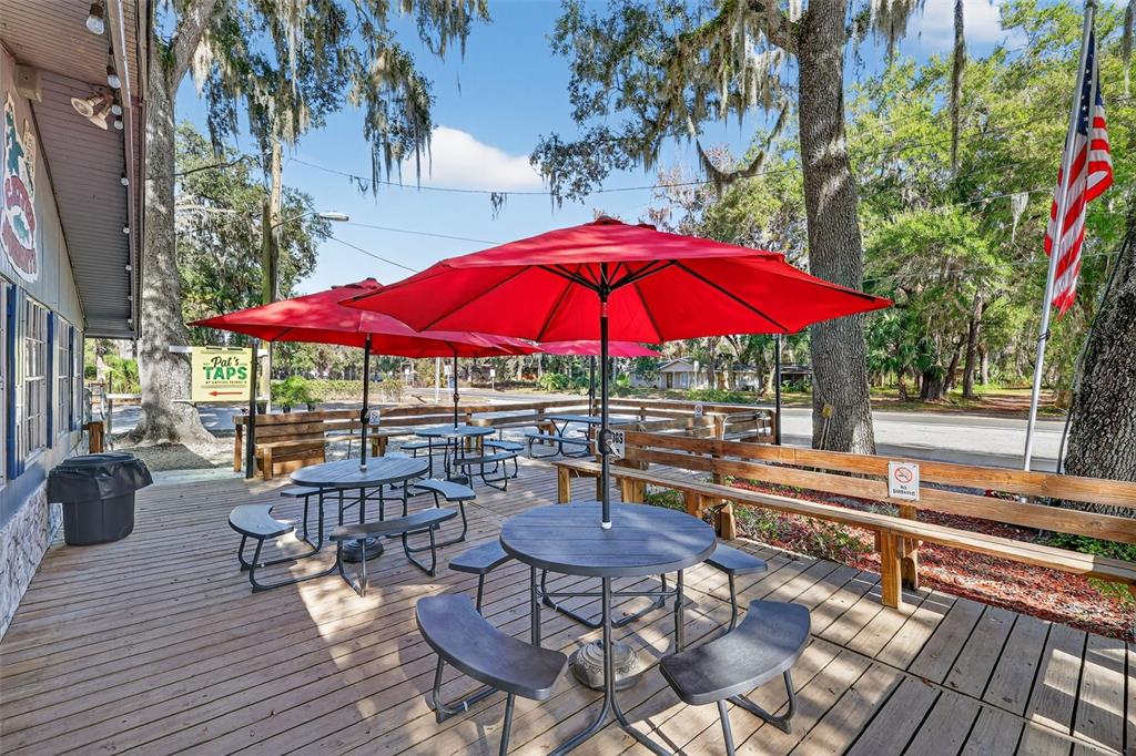 An outdoor wooden deck features several round tables with red umbrellas and bench seating — 2396 N C 470, LAKE PANASOFFKEE, FL