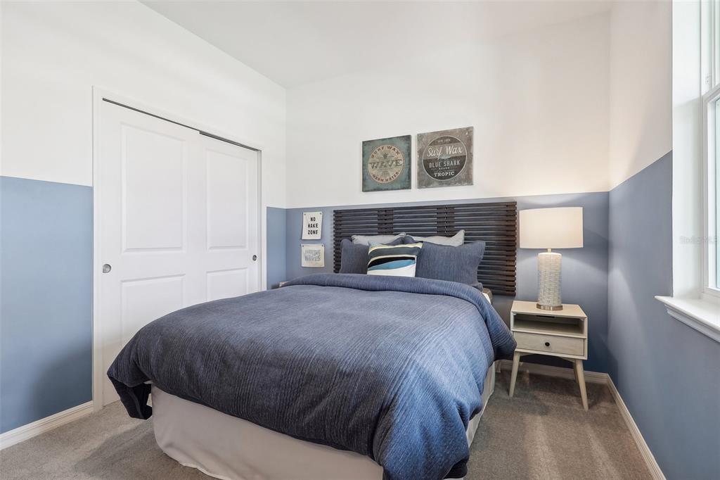 A bedroom features a blue and white color-blocked wall, a bed with blue bedding, and a nightstand — 838 PEBBLE CREST LANE, EAGLE LAKE, FL