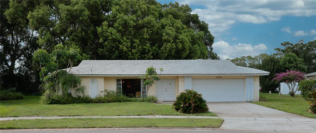 A single-story house with a white tiled roof, a two-car garage, and a landscaped yard — 2132 PORTSIDE PASSAGE, PALM HARBOR, FL