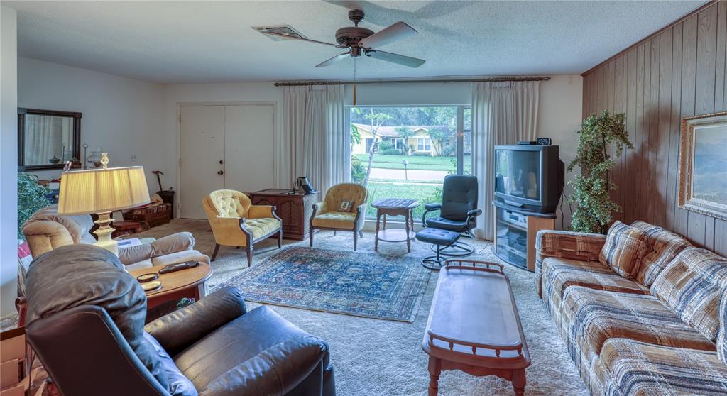 A living room features wood-paneled walls, a large window, a ceiling fan, and various furniture — 2132 PORTSIDE PASSAGE, PALM HARBOR, FL