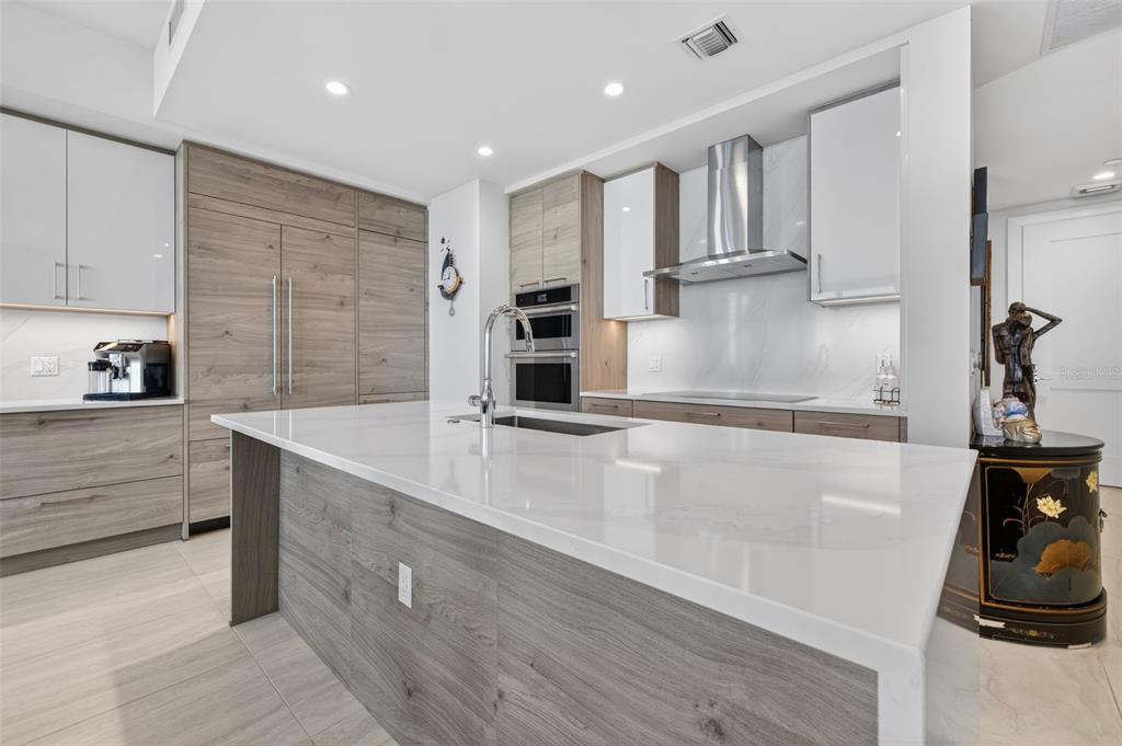 A modern kitchen features a large white quartz island, wood-grain cabinetry, and stainless steel appliances — 301 1ST STREET S UNIT 1505, ST PETERSBURG, FL