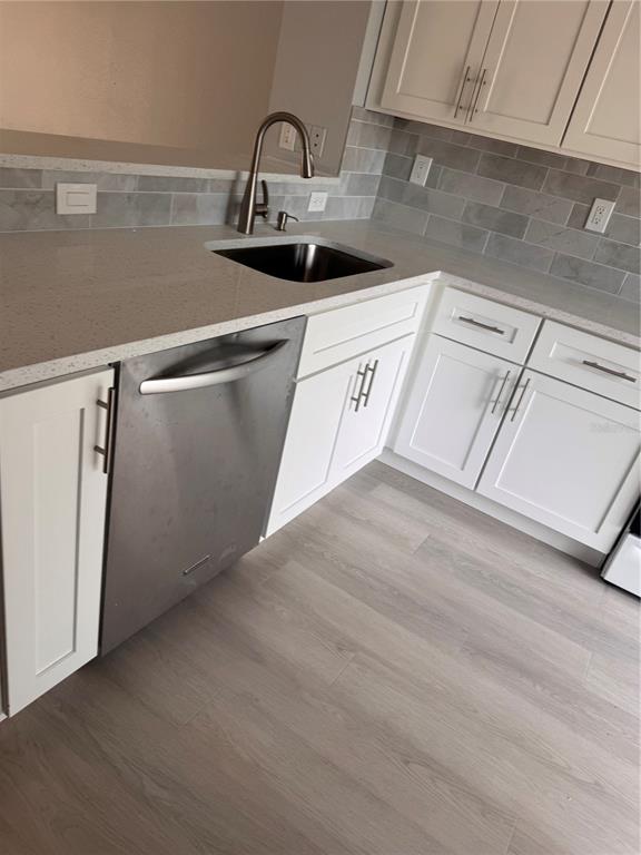 A kitchen features white cabinets, a stainless steel dishwasher, a sink, and gray tile backsplash — 1133 E ROHE STREET UNIT A, TARPON SPRINGS, FL