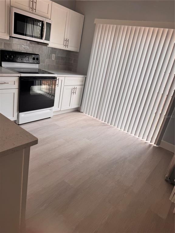 A kitchen features white cabinets, stainless steel appliances, a tiled backsplash, and light wood flooring — 1133 E ROHE STREET UNIT A, TARPON SPRINGS, FL