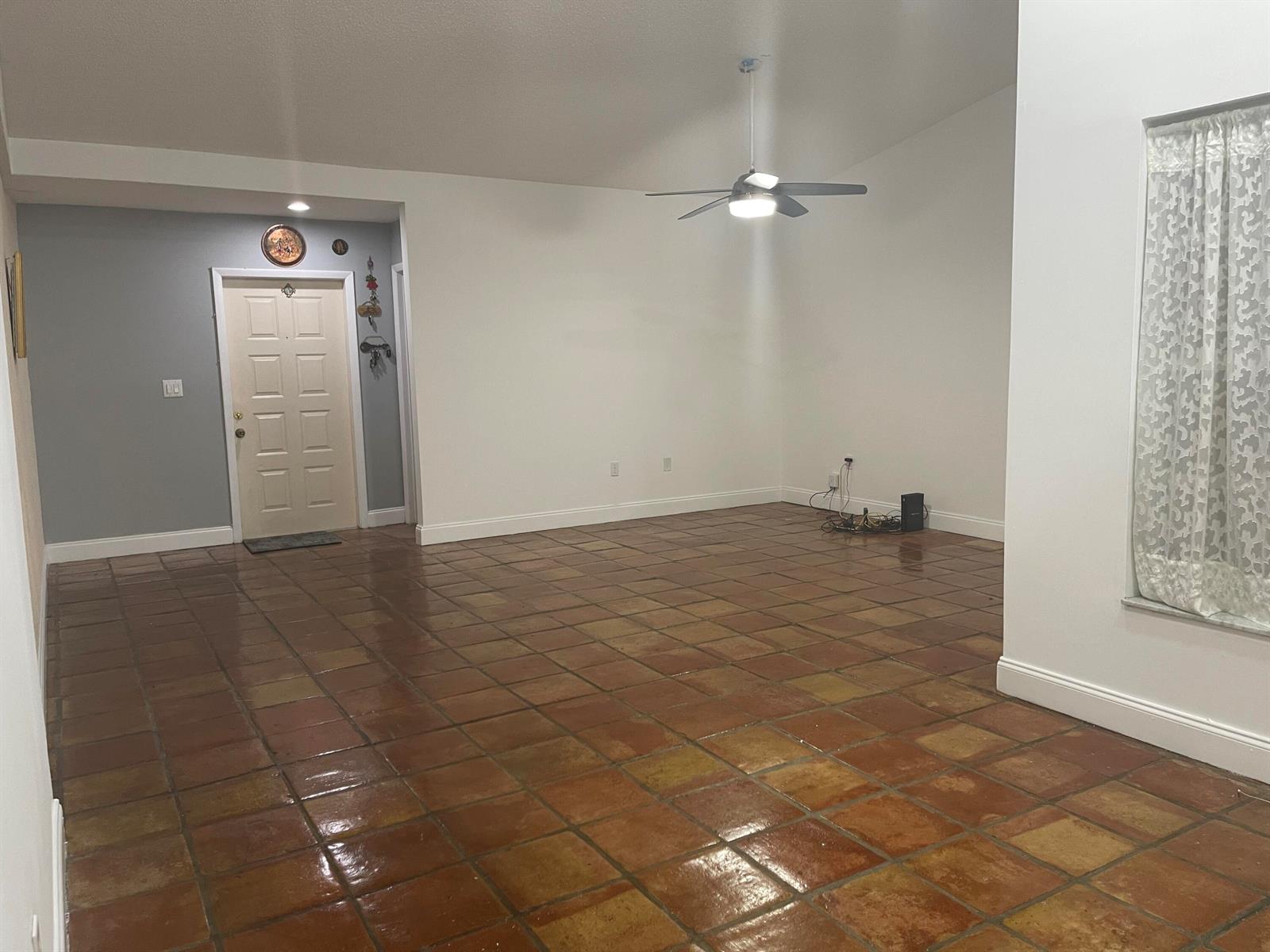 An empty living room features terracotta tile flooring, white walls, and a ceiling fan — 19823 NW 64th Place, Hialeah FL 33015, HIALEAH, FL