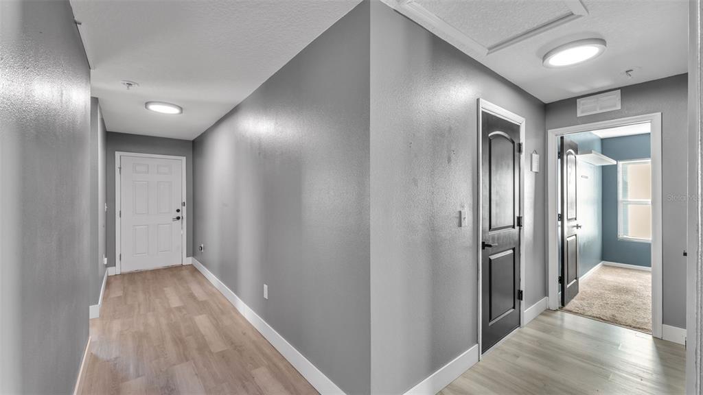 A hallway with gray walls, light wood-look flooring, and two doors leading to other rooms — 1 REDWOOD COURT, KISSIMMEE, FL