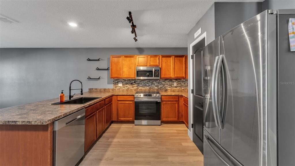 A kitchen features wood cabinets, stainless steel appliances, a dark countertop, and light wood flooring — 1 REDWOOD COURT, KISSIMMEE, FL