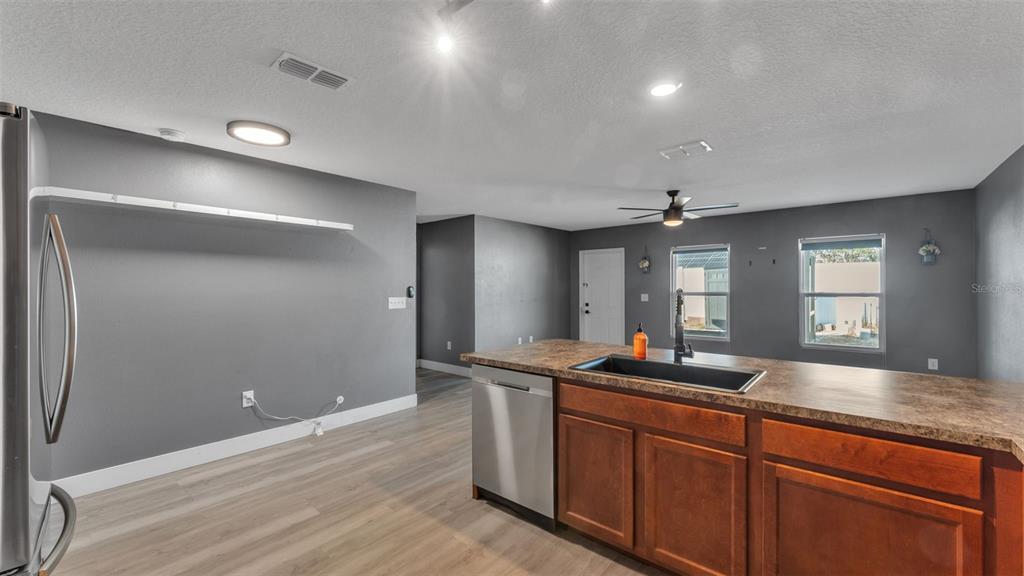 A kitchen features dark gray walls, wood-toned cabinets, a laminate countertop, and light wood flooring — 1 REDWOOD COURT, KISSIMMEE, FL