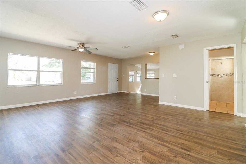 A spacious living room features wood-look flooring, a ceiling fan, and an adjacent bathroom doorway — 2626 15TH AVENUE N, ST PETERSBURG, FL