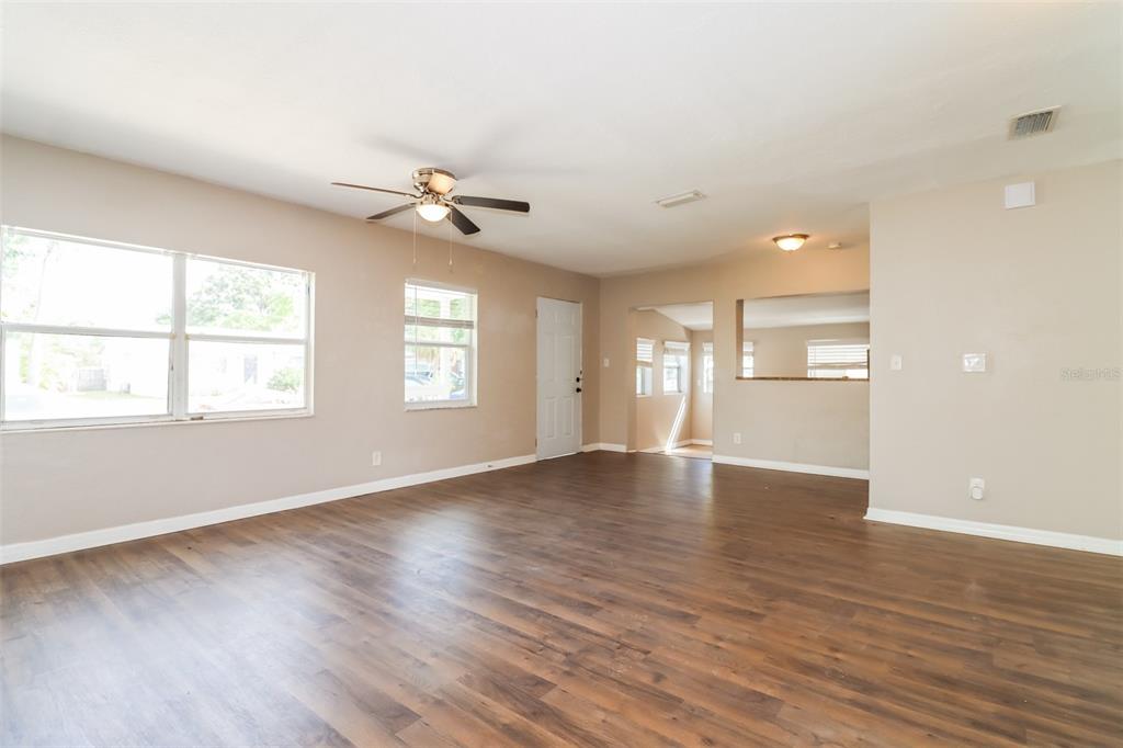 An empty living room features wood-look flooring, beige walls, a ceiling fan, and windows — 2626 15TH AVENUE N, ST PETERSBURG, FL