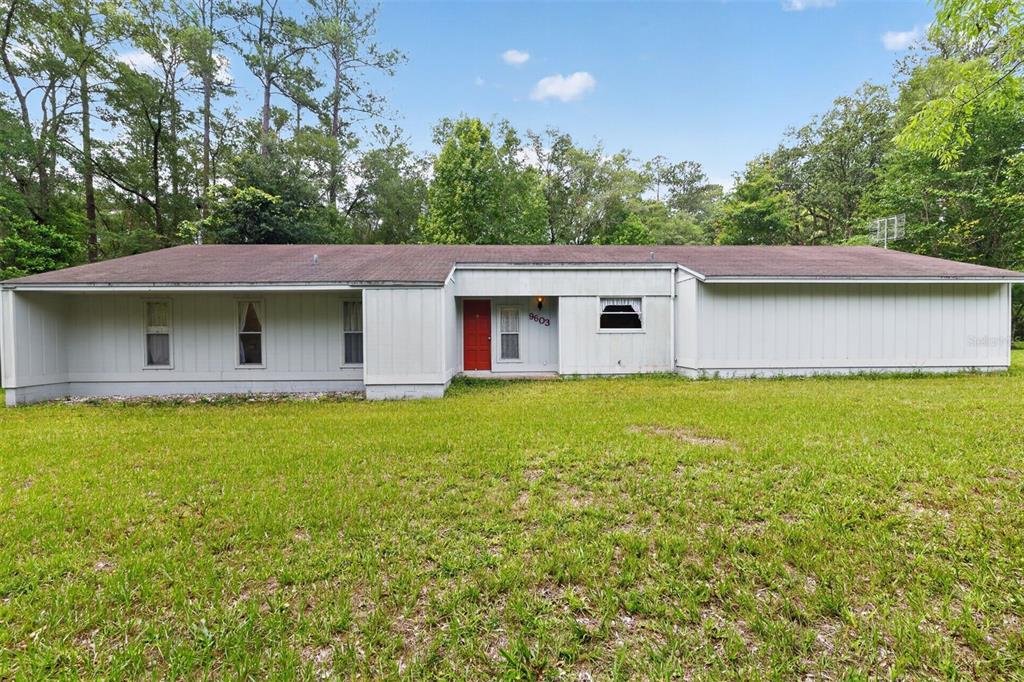 A single-story house with light-colored vertical siding, a red front door, and a brown roof — 9603 SW 17TH AVENUE, GAINESVILLE, FL