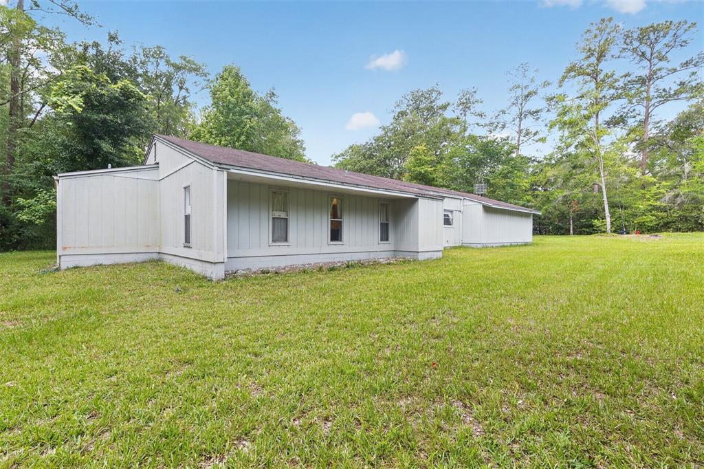 A light-colored, single-story house with vertical siding sits on a large, grassy lawn — 9603 SW 17TH AVENUE, GAINESVILLE, FL