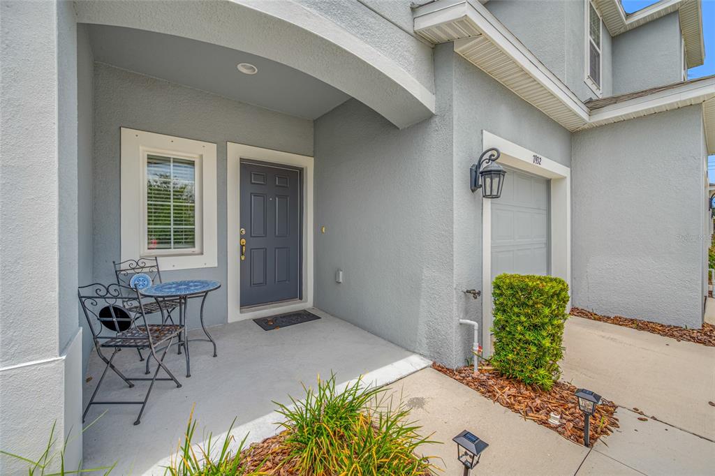 A gray house exterior features a front porch with a small bistro set and door — 7932 EVERGREEN CREEK COURT, RIVERVIEW, FL