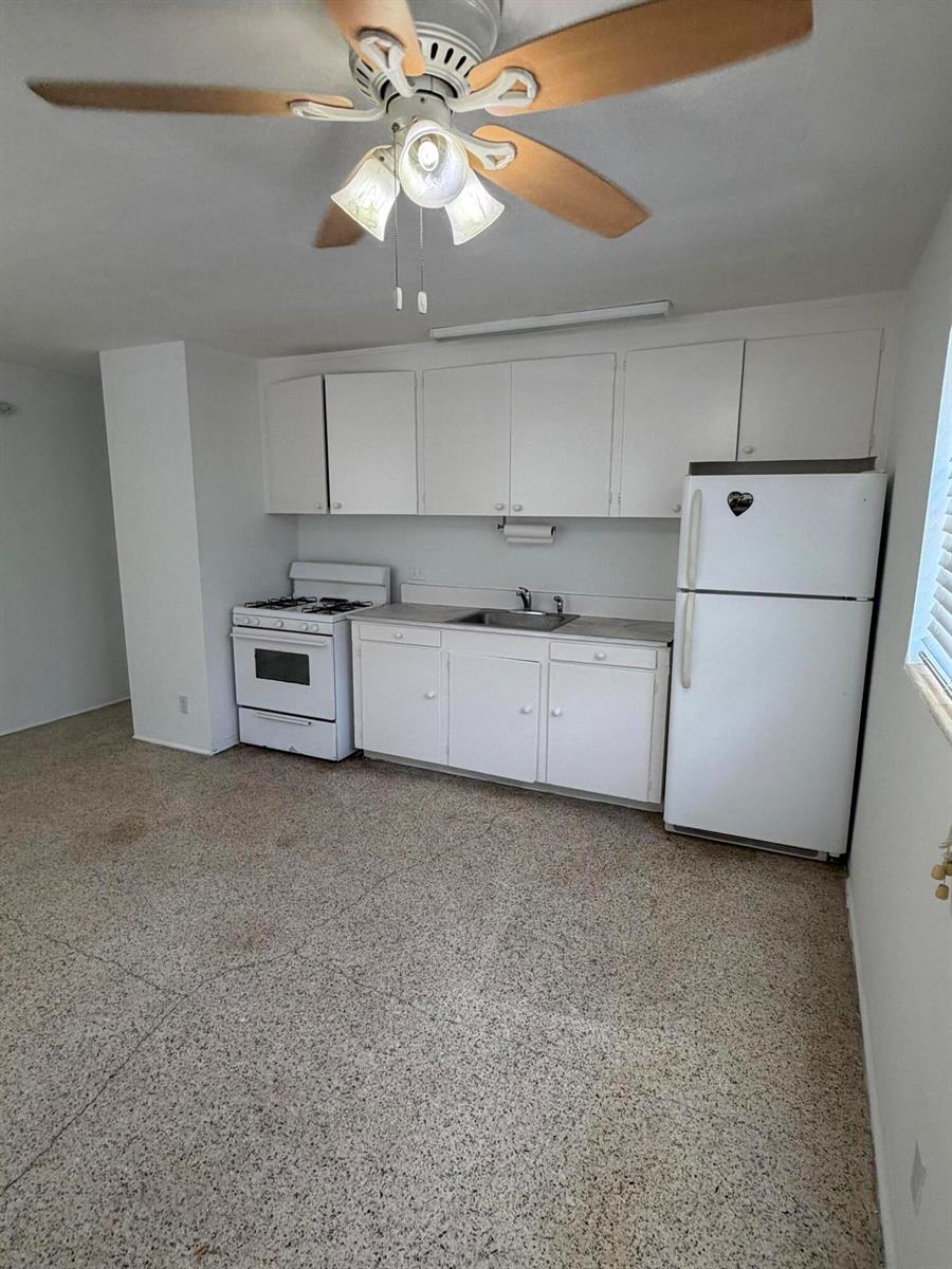A kitchen features white cabinets, a white stove, a refrigerator, and speckled flooring — WEST PALM BEACH, FL