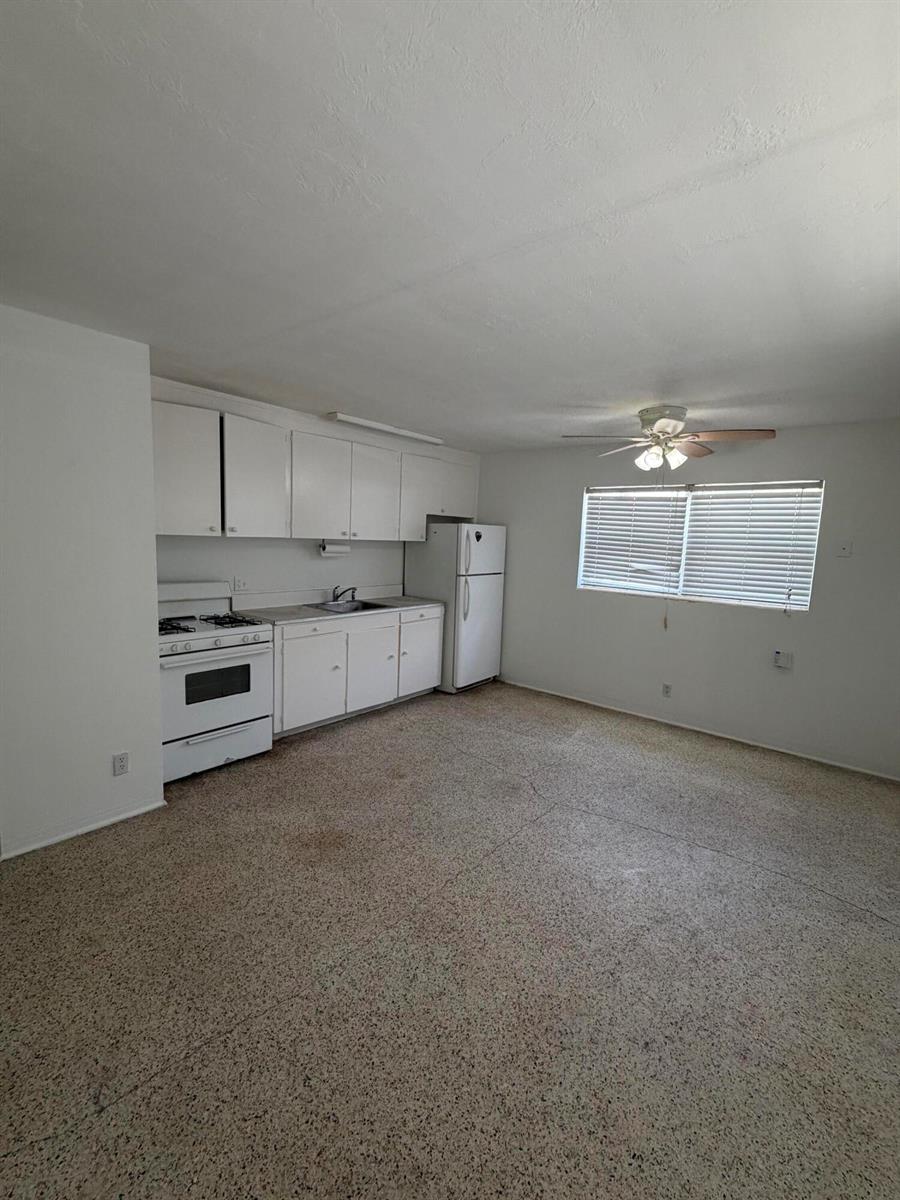 A kitchen with white cabinets, a white stove, a refrigerator, and speckled flooring — WEST PALM BEACH, FL