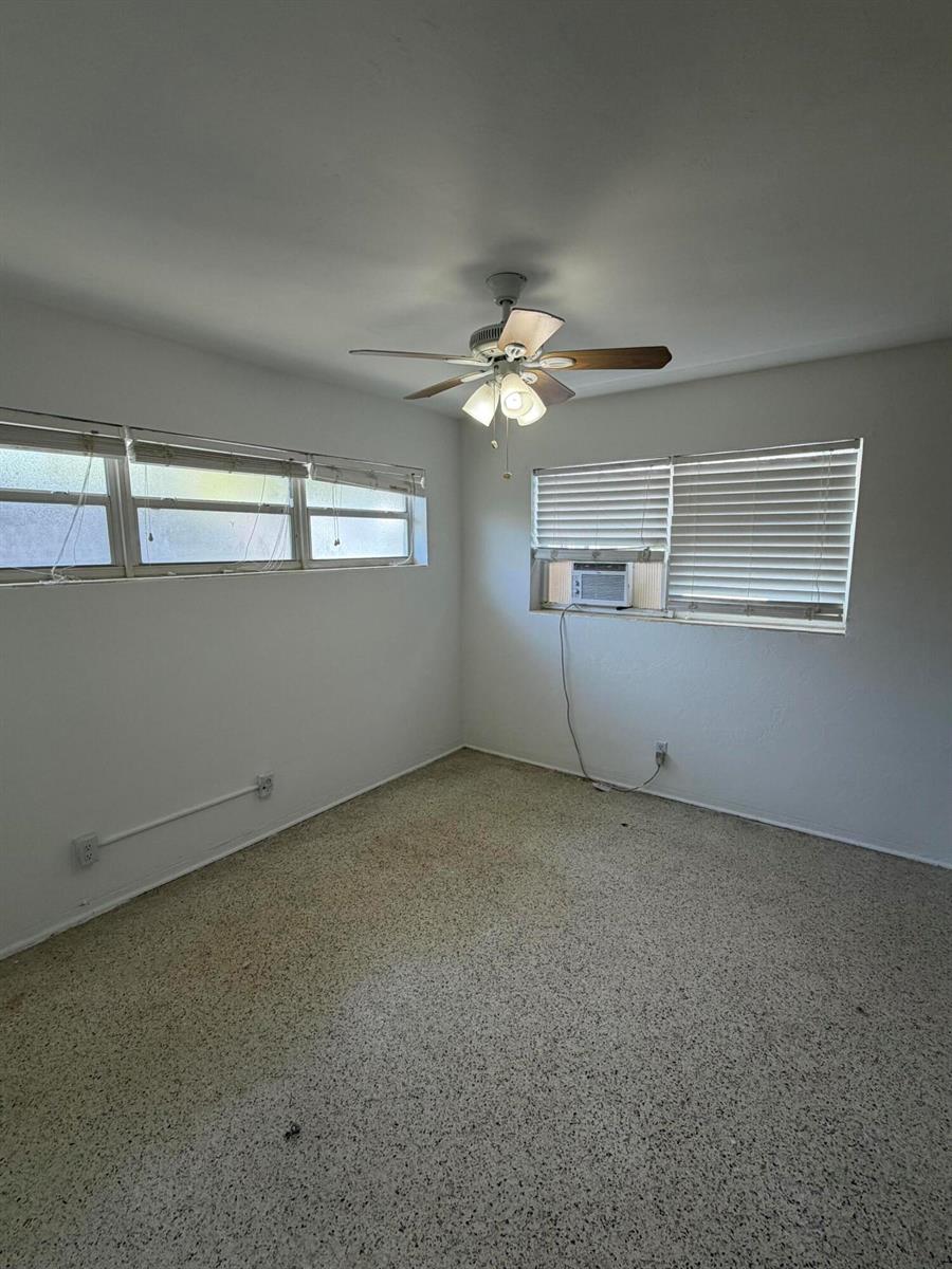 An empty room features a ceiling fan, window blinds, a wall-mounted air conditioner, and terrazzo flooring — WEST PALM BEACH, FL