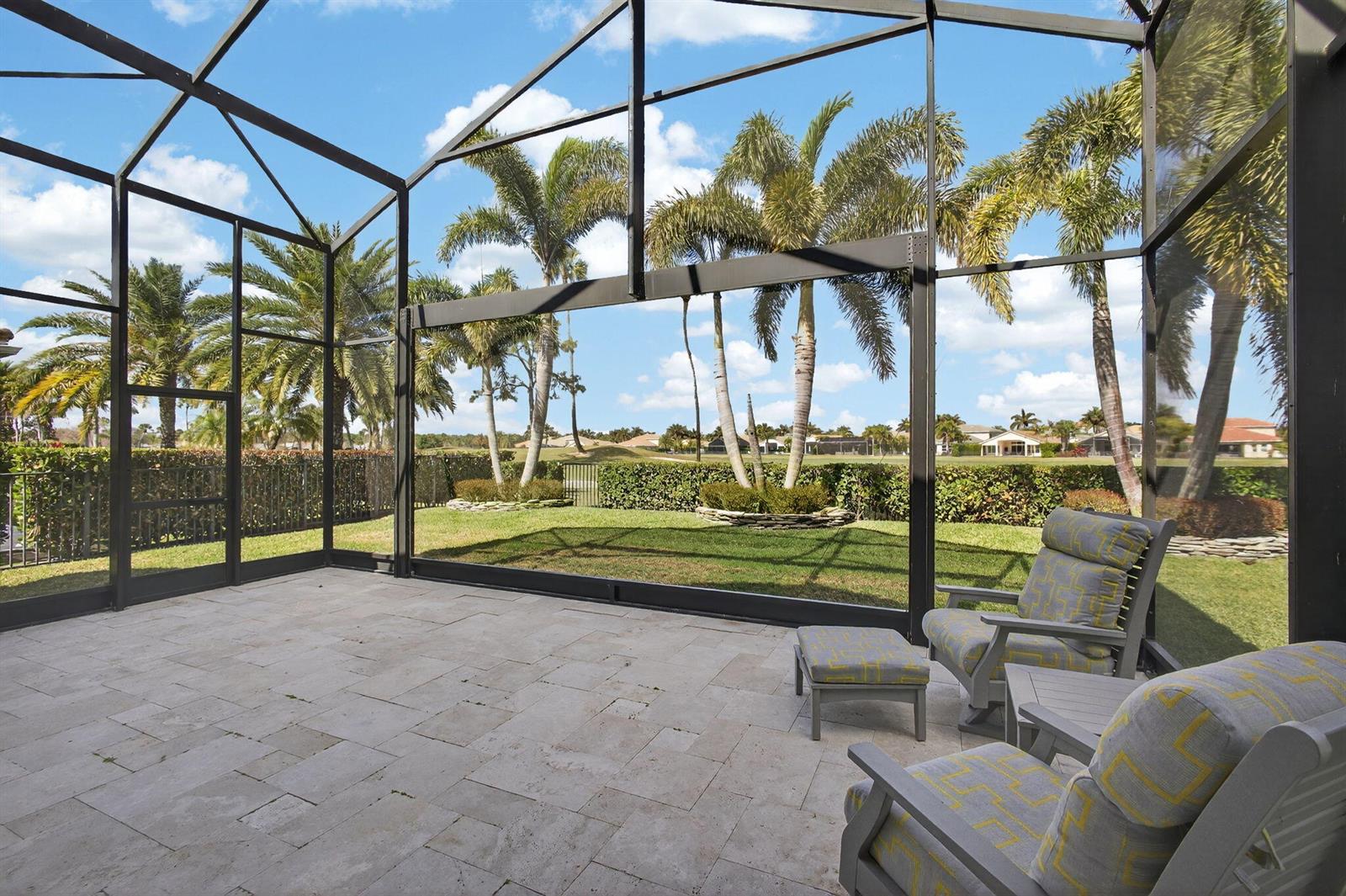 A screened-in patio with stone flooring overlooks a grassy yard, palm trees, and a golf course — 157 Carina Drive, Jupiter FL 33478, JUPITER, FL