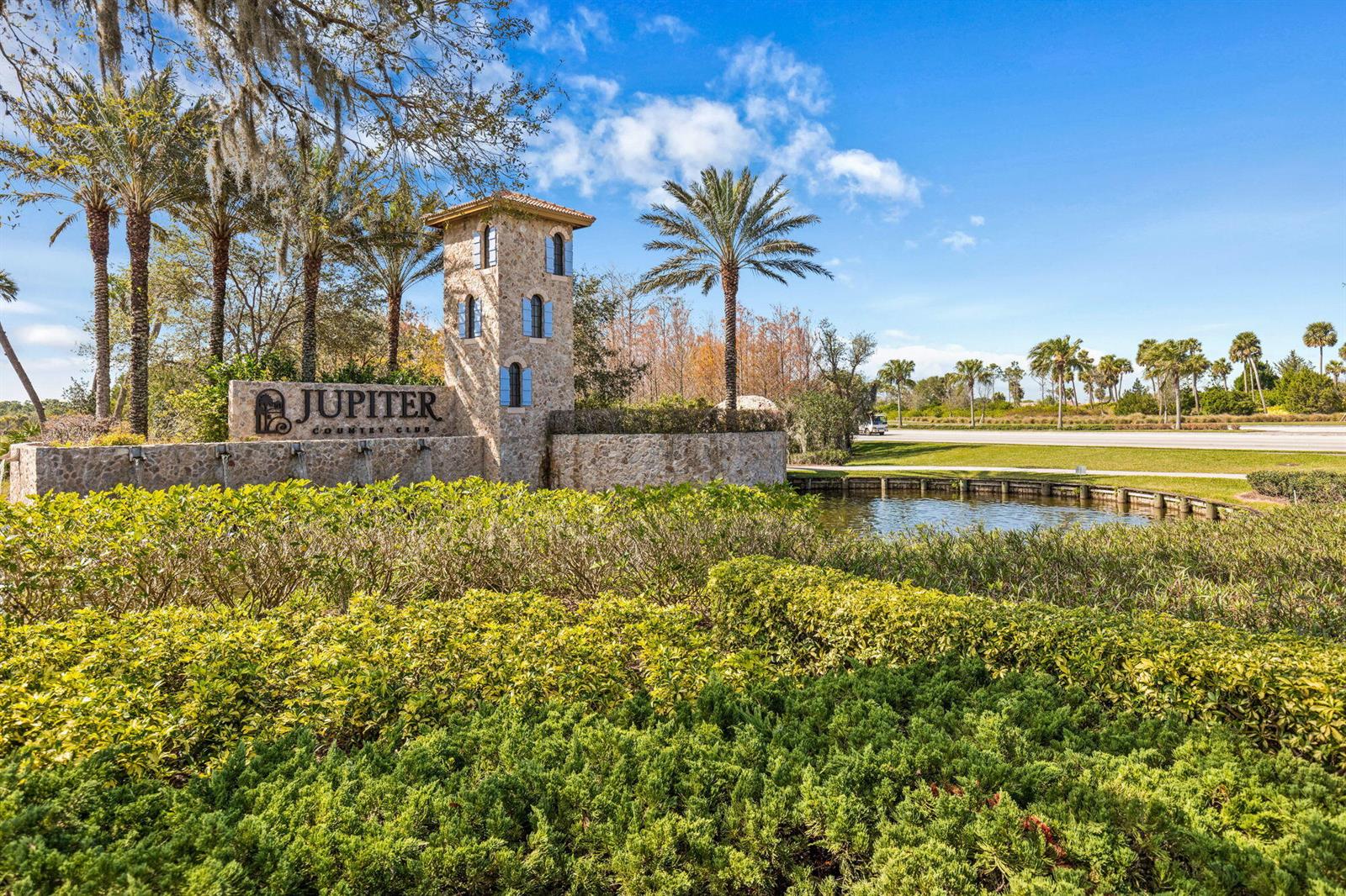 A stone monument sign for Jupiter Country Club stands beside a pond and palm trees — 157 Carina Drive, Jupiter FL 33478, JUPITER, FL