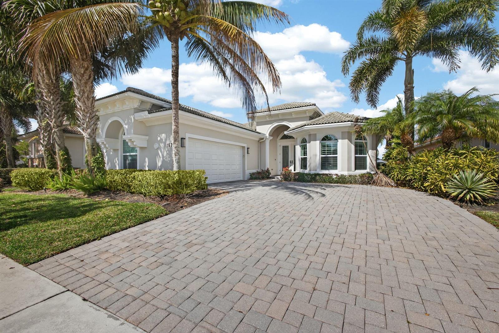 A single-story house with a paved driveway, a two-car garage, and several palm trees — 157 Carina Drive, Jupiter FL 33478, JUPITER, FL