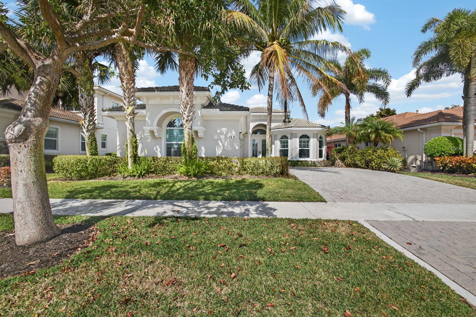 A single-story house with a paved driveway, palm trees, and a manicured lawn — 157 Carina Drive, Jupiter FL 33478, JUPITER, FL