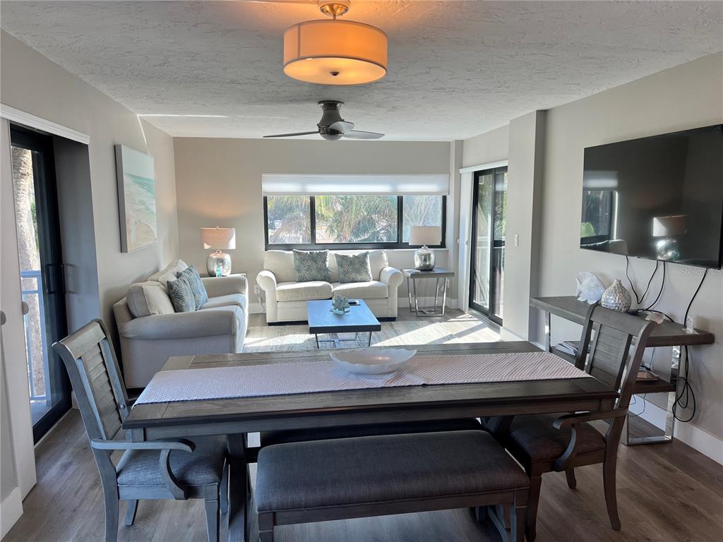 A dining area and living room feature wood-look flooring, neutral walls, and large windows — 1001 POINT OF ROCKS ROAD UNIT 208, SARASOTA, FL