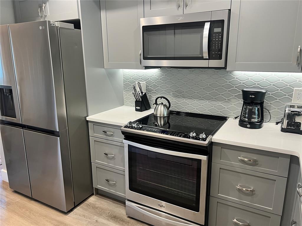 A kitchen features gray cabinets, stainless steel appliances, a white countertop, and a tiled backsplash — 1001 POINT OF ROCKS ROAD UNIT 208, SARASOTA, FL