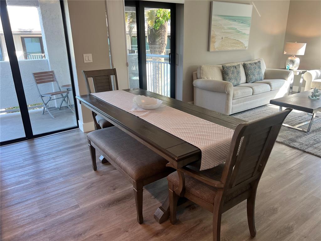 A dining area with a wooden table and bench sits beside a living room — 1001 POINT OF ROCKS ROAD UNIT 208, SARASOTA, FL