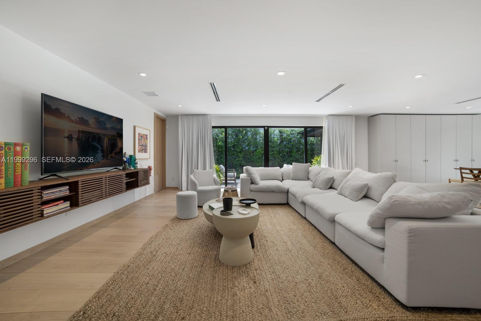 A modern living room features a large white sectional sofa, a wall-mounted media console, and floor-to-ceiling windows — 70 Samana Dr, Miami FL 33133, MIAMI, FL