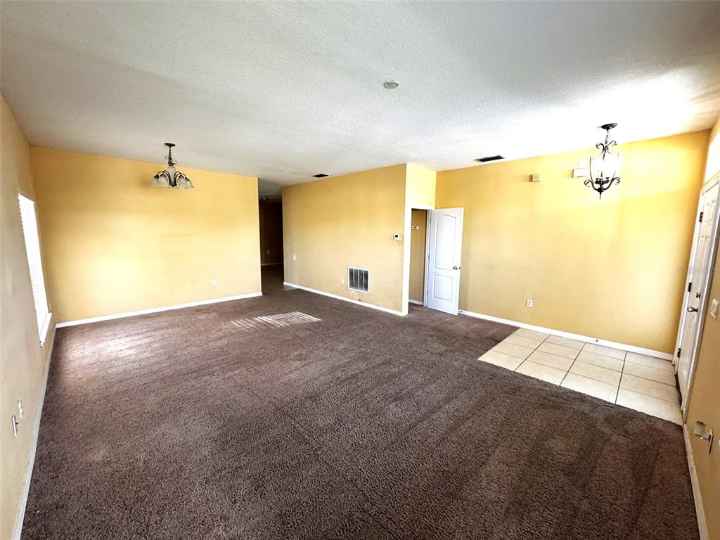 A spacious living room features yellow walls, brown carpeting, two chandeliers, and a tiled entryway — 1111 HACIENDA CIRCLE, KISSIMMEE, FL