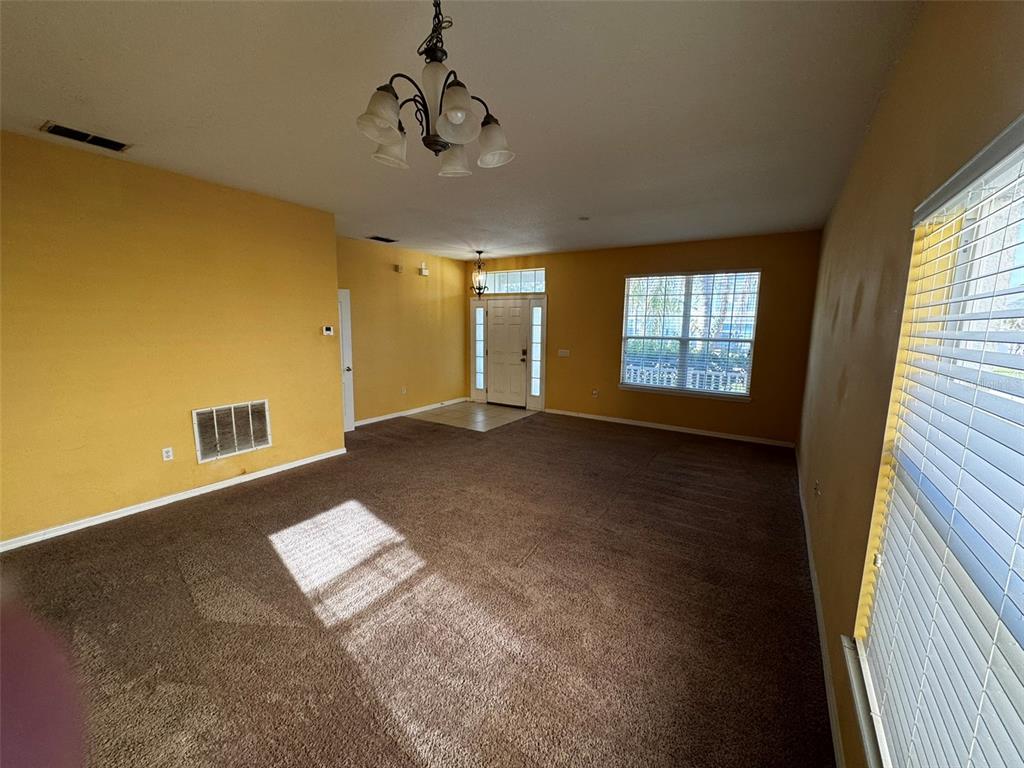 An empty living room features yellow walls, brown carpeting, a chandelier, and a front entrance — 1111 HACIENDA CIRCLE, KISSIMMEE, FL