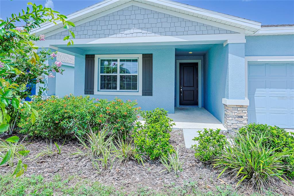 A light blue house exterior features a dark front door, stone accents, and landscaping — 516 REGGIE ROAD, WINTER HAVEN, FL