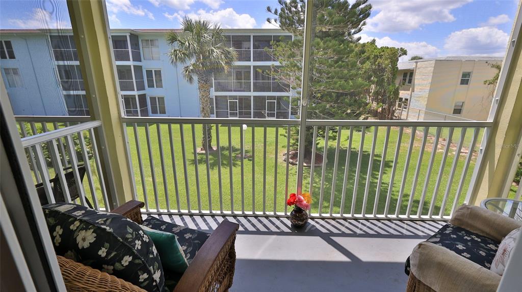 A screened-in balcony overlooks a grassy courtyard with palm trees and neighboring apartment buildings — 717 S BEACH STREET UNIT 205C, DAYTONA BEACH, FL