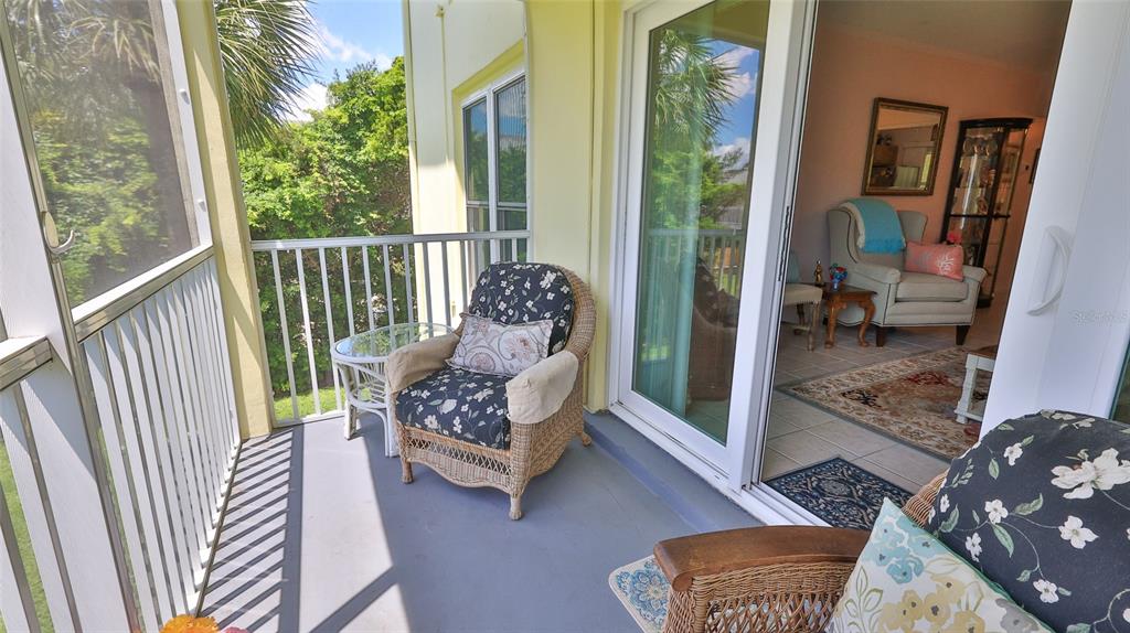 A screened-in balcony features wicker chairs with floral cushions and a view of trees — 717 S BEACH STREET UNIT 205C, DAYTONA BEACH, FL