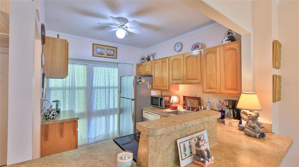 A kitchen features light wood cabinets, laminate countertops, a ceiling fan, and a sliding glass door — 717 S BEACH STREET UNIT 205C, DAYTONA BEACH, FL
