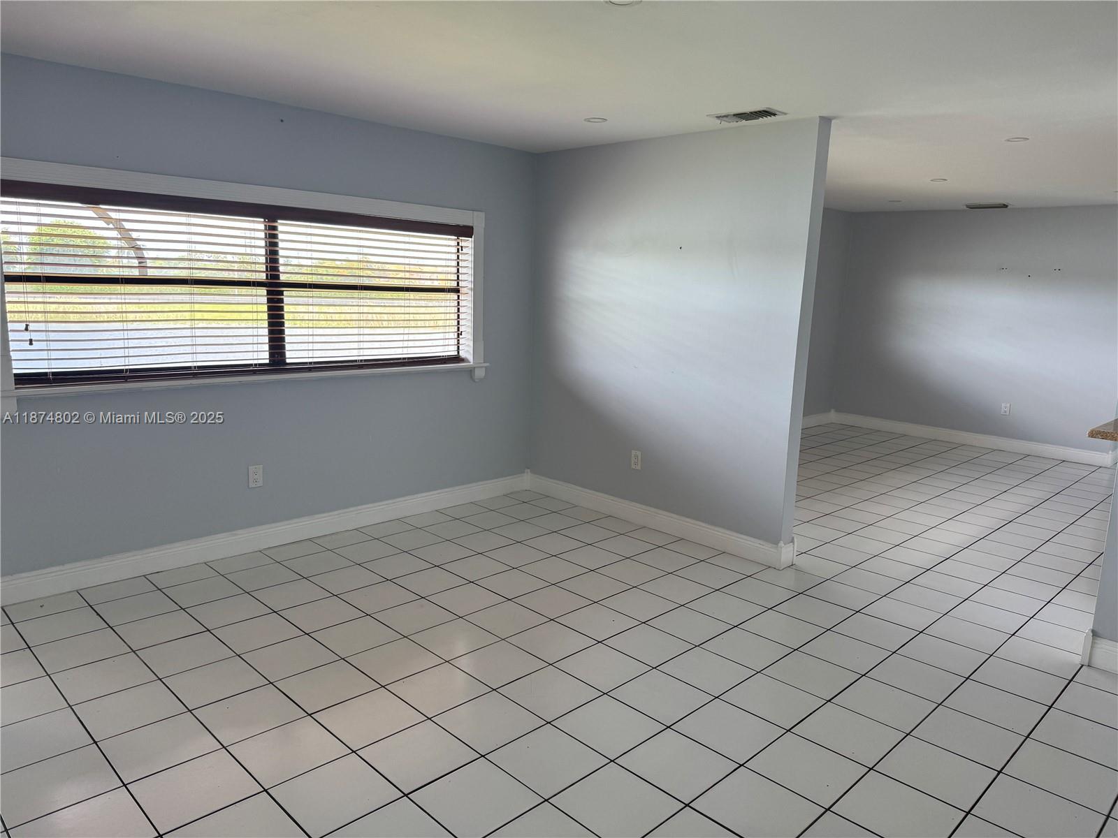 An empty room features white tiled floors, light blue walls, and a large window — 13261 SW 17th Ln # 5, Miami FL 33175, MIAMI, FL