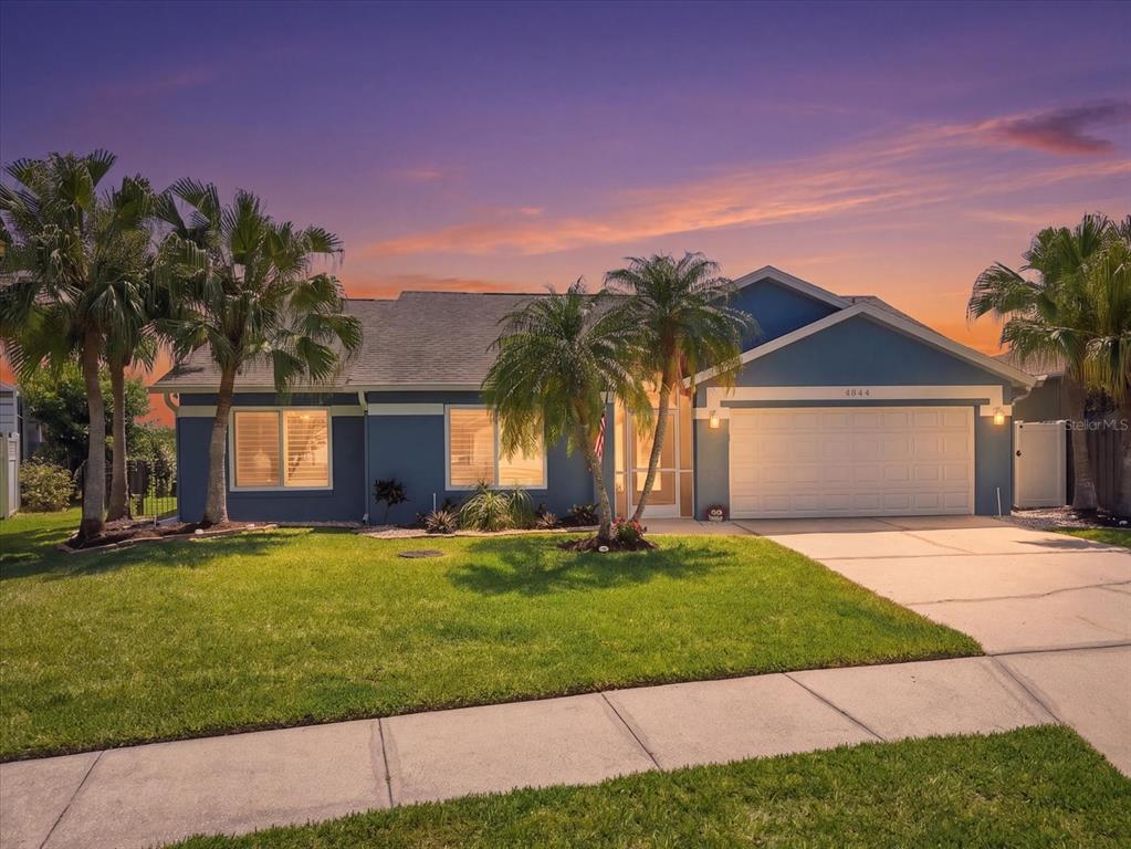A blue single-story house with a two-car garage and palm trees at sunset — 4844 14TH AVENUE E, BRADENTON, FL