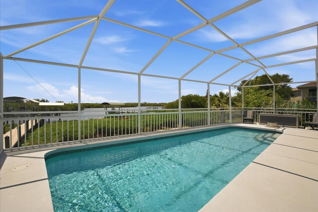 A screened-in swimming pool overlooks a canal with boat docks under a blue sky — 4844 14TH AVENUE E, BRADENTON, FL